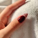 Dettaglio di manicure gel bordeaux con accent nail decorata a spirale